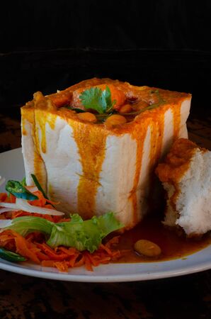 A Durban Bunny Chow - or, in this case, a vegerarian quarter bean bunny - served with sambals. This is an iconic Durban meal consisting of a section of a loaf of bread hollowed out and filled with bean curry and gravy. The sambals are grated carrot with chopped chilli. The meal is traditionally eaten with one's fingers.の写真素材