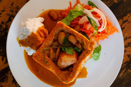 A Durban Bunny Chow - or, in this case, a vegerarian quarter bean bunny - served with sambals. This is an iconic Durban meal consisting of a section of a loaf of bread hollowed out and filled with bean curry and gravy. The sambals are grated carrot with chopped chilli. The meal is traditionally eaten with one's fingers.の写真素材
