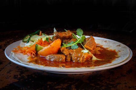 A mutton curry roti with sambals - an iconic Durban meal consisting of a roti topped with mutton curry and gravy. The sambals are grated carrot with chopped chilli.の写真素材