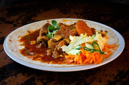 A mutton curry roti with sambals - an iconic Durban meal consisting of a roti topped with mutton curry and gravy. The sambals are grated carrot with chopped chilli.の写真素材