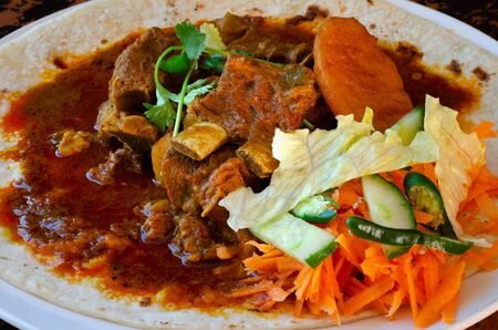 A mutton curry roti with sambals - an iconic Durban meal consisting of a roti topped with mutton curry and gravy. The sambals are grated carrot with chopped chilli.の写真素材