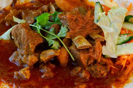 A mutton curry roti with sambals - an iconic Durban meal consisting of a roti topped with mutton curry and gravy. The sambals are grated carrot with chopped chilli.の写真素材