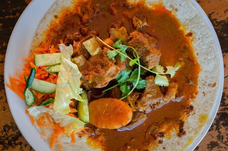 A mutton curry roti with sambals - an iconic Durban meal consisting of a roti topped with mutton curry and gravy. The sambals are grated carrot with chopped chilli.の写真素材