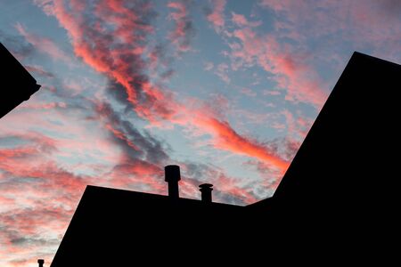 Black silhouette of the roof of a house with two chimneys and a pinkish blue sky