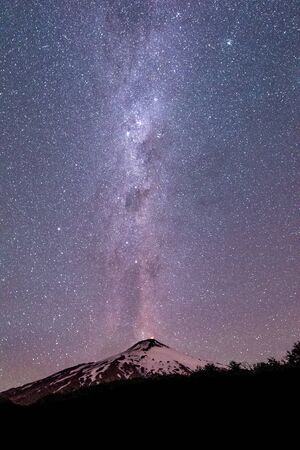 Thousands of stars in the sky with the Milky Way above the Villarrica Volcano in Chile, vertical...