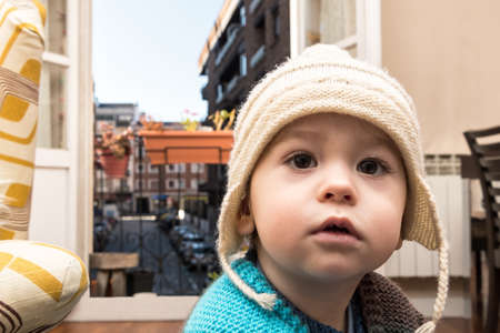 Baby about one year old, looking out from the balcony in the confinement, wearing a wool capの写真素材
