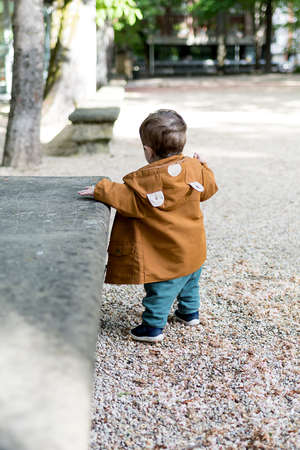 A year and a half old baby taking his first steps in a park with a loose stone floor, he is learning to walkの写真素材