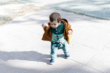 A year and a half old baby taking his first steps in a park with a loose stone floor, he is learning to walkの写真素材