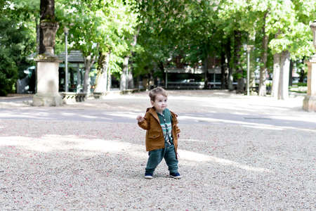 A year and a half old baby taking his first steps in a park with a loose stone floor, he is learning to walkの写真素材