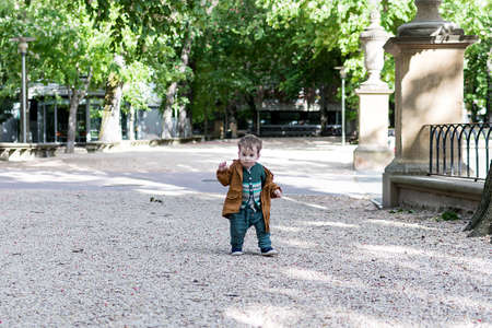 A year and a half old baby taking his first steps in a park with a loose stone floor, he is learning to walkの写真素材