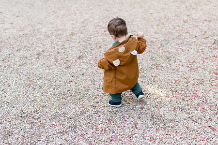 A year and a half old baby taking his first steps in a park with a loose stone floor, he is learning to walkの写真素材