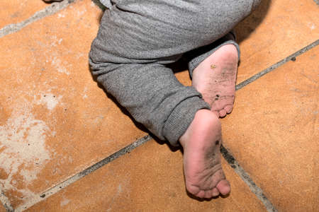 Dirty feet of a year and a half old boy who is kneeling on the floor of his terraceの写真素材