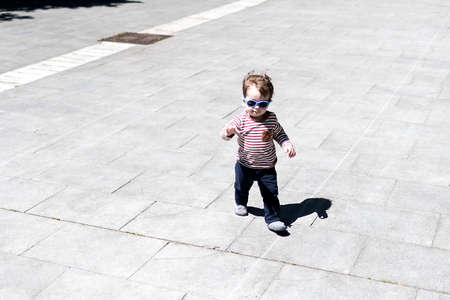 A year and a half old boy walking down the street with blue sunglasses onの写真素材