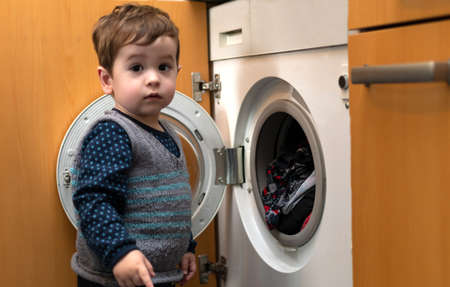 Child helping to set up the washing machine to do the laundry. He puts the clothes in the vat.の写真素材
