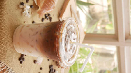 Ice coffee and milk in takeaway cup with shell-shaped and coffee bean background.の写真素材