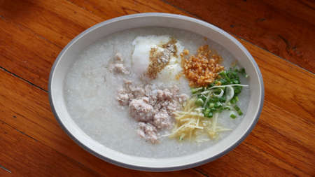 Asian congee with ground pork, egg and vegetable in a bowl on wooden background.の写真素材