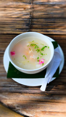 Congee with shrimp top with vegetable and edible flower in bowl.
