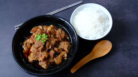 Top view pork stew (braised) in black bowl with steam white rice on black background.の写真素材