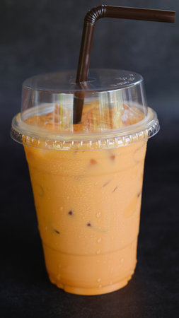 Ice Thai tea with milk in plastic to go cup on black background.の写真素材