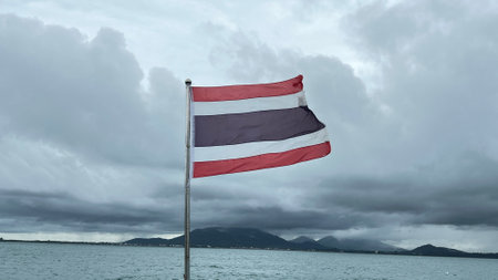 Thai flag blowing in the wind with the sea and storm cloud background.の写真素材