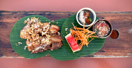 Garlic pork belly with sipcy sauce and salad on banana leaf on wooden table (top view table food set).の写真素材