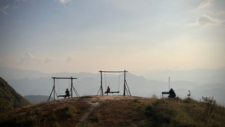 Silhouette of people sitting on a swing at the top of the mountain with sunrise.の写真素材