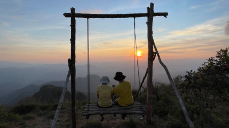 Silhouette couple sitting on a swing at sunset on the mountains,Thailand.の写真素材