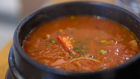 Close up of spicy tomato soup in black bowl on wooden table.