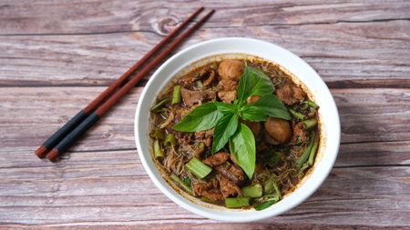 Thai style noodle soup with pork and green basil in a bowl with chopsticks on black backgroundの写真素材