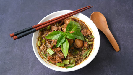 Thai style noodle soup with pork and green basil in a bowl with chopsticks on black backgroundの写真素材