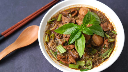 Thai style noodle soup with pork and green basil in a bowl with chopsticks on black backgroundの写真素材