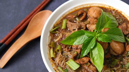 Thai style noodle soup with pork and green basil in a bowl with chopsticks on black backgroundの写真素材