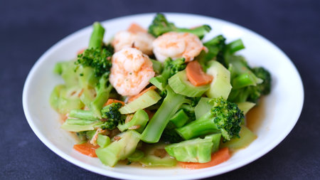 table top view stir-fried broccoli with shrimp and carrot in white plate isolated on black background.の写真素材