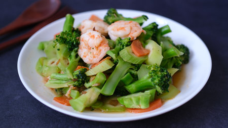 table top view stir-fried broccoli with shrimp and carrot in white plate isolated on black background.の写真素材