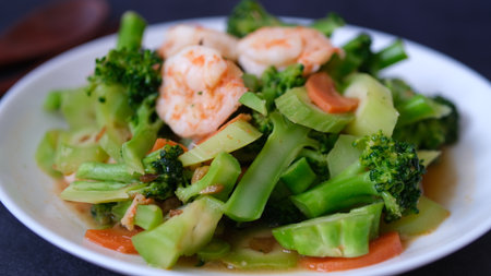 table top view stir-fried broccoli with shrimp and carrot in white plate isolated on black background.の写真素材