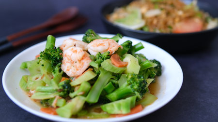 table top view stir-fried broccoli with shrimp and carrot in white plate isolated on black background.の写真素材