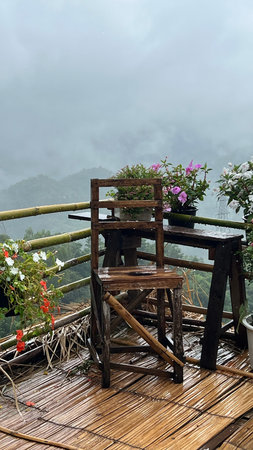 Wooden table and chair with flowers on terrace in rainy day with mountain background.の写真素材