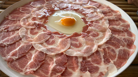 Slices of pork on a plate with a fresh egg.の写真素材
