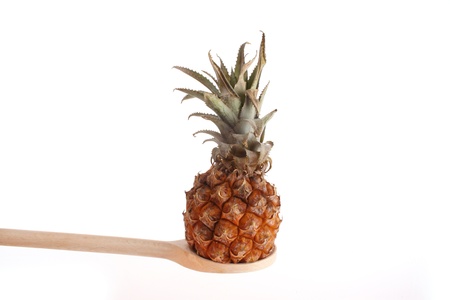 Pineapple on a wooden spoon isolated against a white background