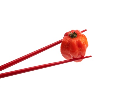 Chopsticks holding a pepper against white backgroundの写真素材