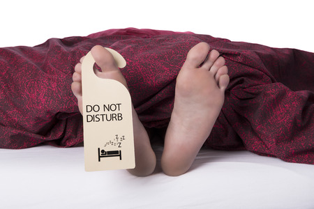 Two feet sticking out from sheets with a do not disturb label on a toe on a white backgroundの写真素材