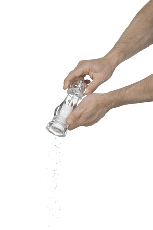 Two male hands using a salt grinder creating a flow of crushed salt to add flavor to food on a white backgroundの写真素材