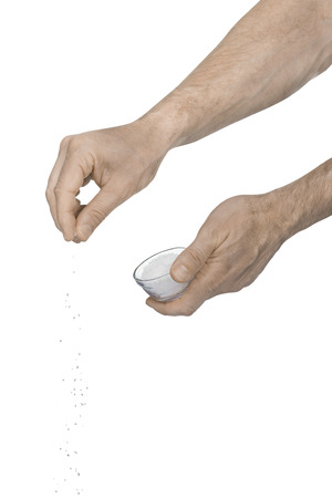 Two caucasian male hands adding crushed salt from a glass cup using finger tips to add flavor to food on a white backgroundの写真素材