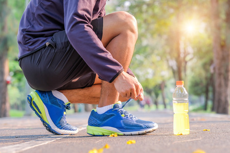 Young athlete man tying running shoes in the park outdoor, male runner ready for jogging on the road outside, asian Fitness walking and exercise on footpath in morning. wellness and sport conceptsの写真素材
