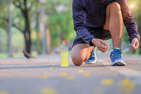 Young athlete man tying running shoes in the park outdoor, male runner ready for jogging on the road outside, asian Fitness walking and exercise on footpath in morning. wellness and sport conceptsの写真素材