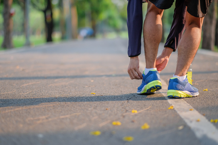 Young athlete man tying running shoes in the park outdoor, male runner ready for jogging on the road...