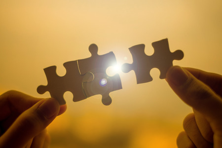 Silhouette Woman hands connecting couple puzzle piece against sunrise effect, businesswoman holding jigsaw with sunset background. Business solutions, target, success, goals and strategy conceptsの写真素材