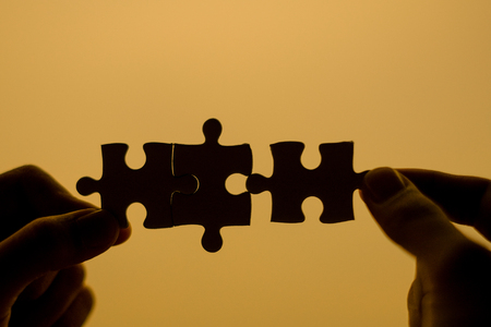 Silhouette Woman hands connecting couple puzzle piece against sunrise effect, businesswoman holding jigsaw with sunset background. Business solutions, target, success, goals and strategy conceptsの写真素材