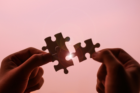 Silhouette Woman hands connecting couple puzzle piece against sunrise effect, businesswoman holding jigsaw with sunset background. Business solutions, target, success, goals and strategy conceptsの写真素材