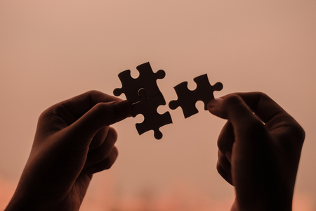 Silhouette Woman hands connecting couple puzzle piece against sunrise effect, businesswoman holding jigsaw with sunset background. Business solutions, target, success, goals and strategy conceptsの写真素材